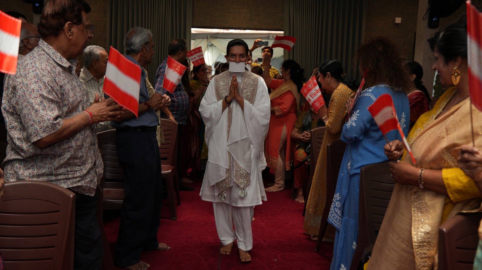 A diksharthi welcomed into the Jain Sangh hall as the sangh waves flags